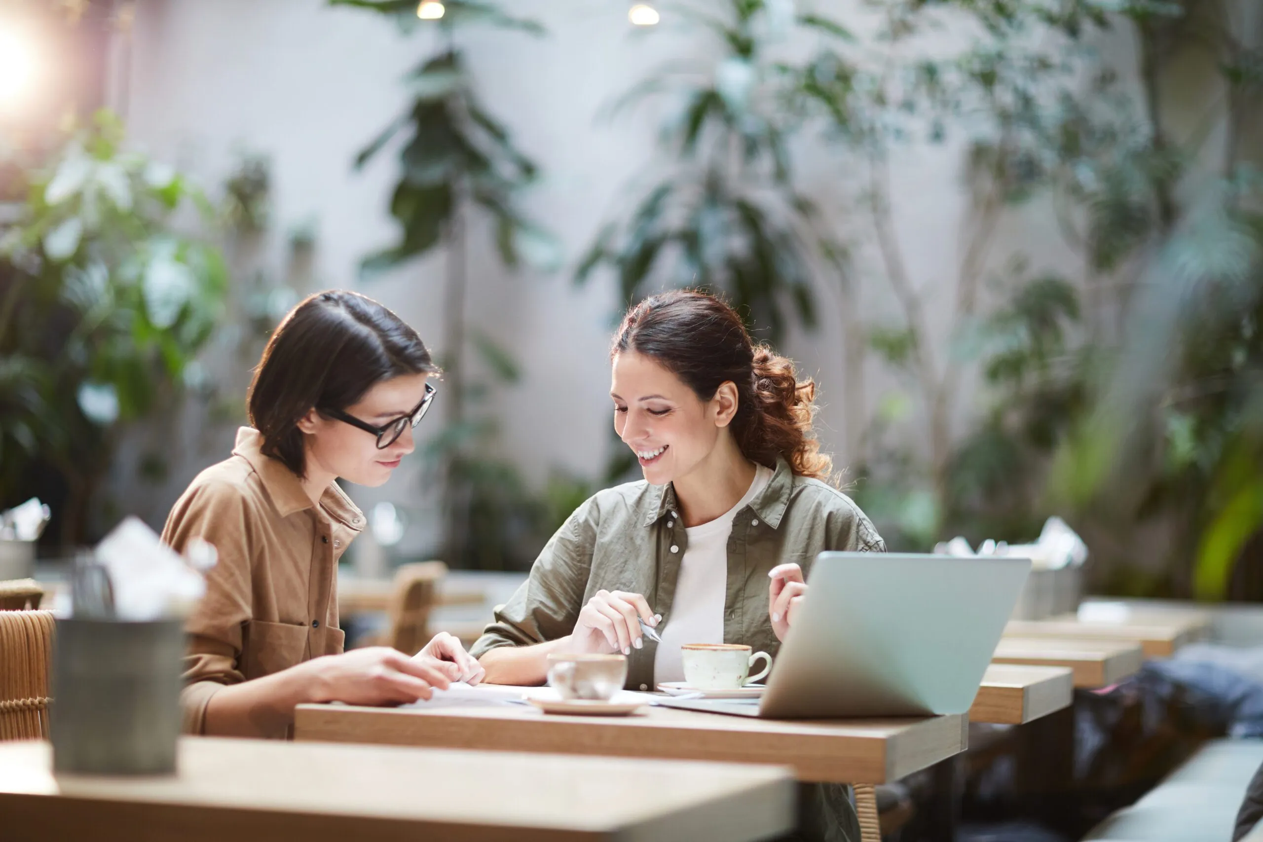 Two women smiling as they work through paperwork at a laptop