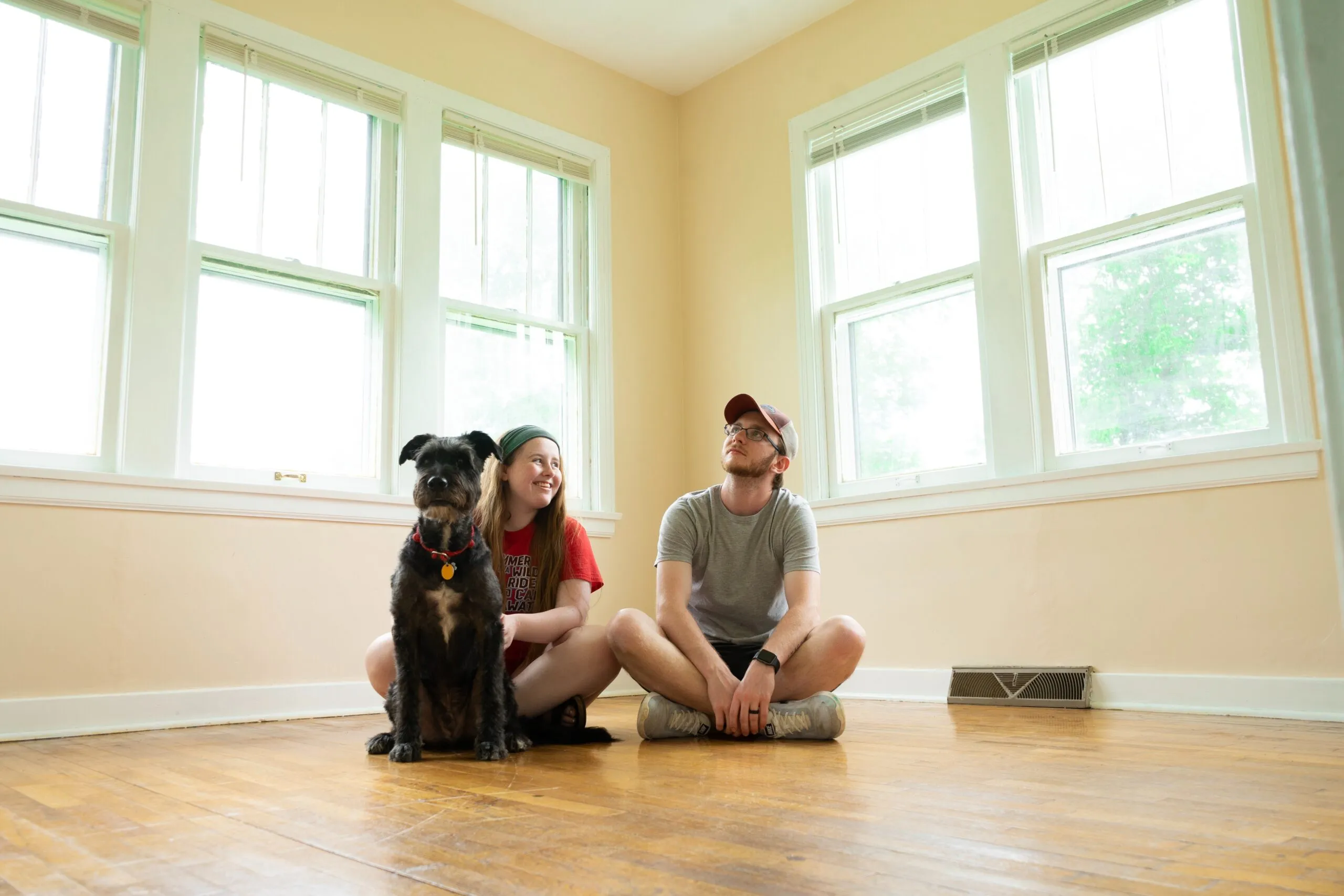 A young couple and their dog sitting on the floor of an empty room in their new home