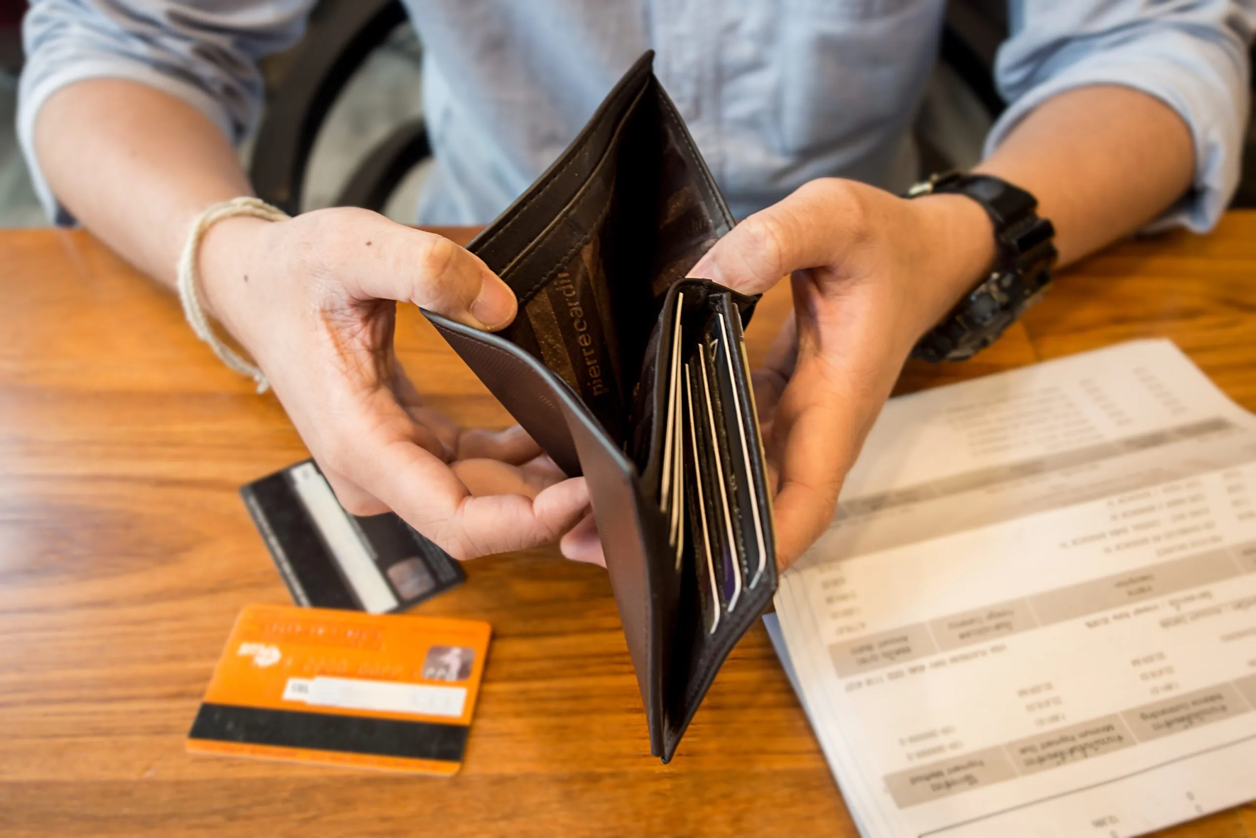 Hands opening an empty wallet beside a credit card and a bill